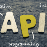 Creative wooden letter illustration of 'API' on a dark wooden background, with annotations explaining its components: 'A' for Application, 'P' for Programming, and 'I' for Interface, demonstrating how APIs connect applications through programming interfaces